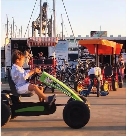 Criança a conduzir um kart a pedal verde na pista, junto à doca