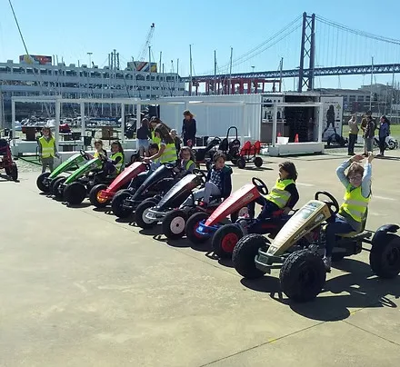 Crianças de colete reflector em karts a pedal, com a Ponte 25 de Abril ao fundo
