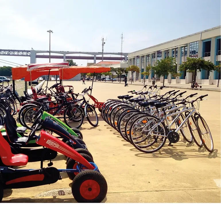Bicicletas e karts a pedal alinhados na pista, com a Ponte 25 de Abril ao fundo