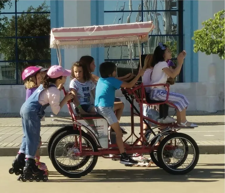 Crianças a pedalar um kart familiar de quatro lugares, acompanhadas de patinadoras