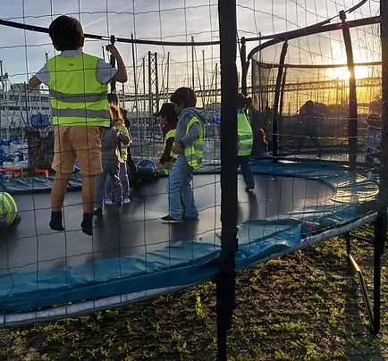 Crianças a saltar no trampolim ao pôr do sol, com a marina ao fundo